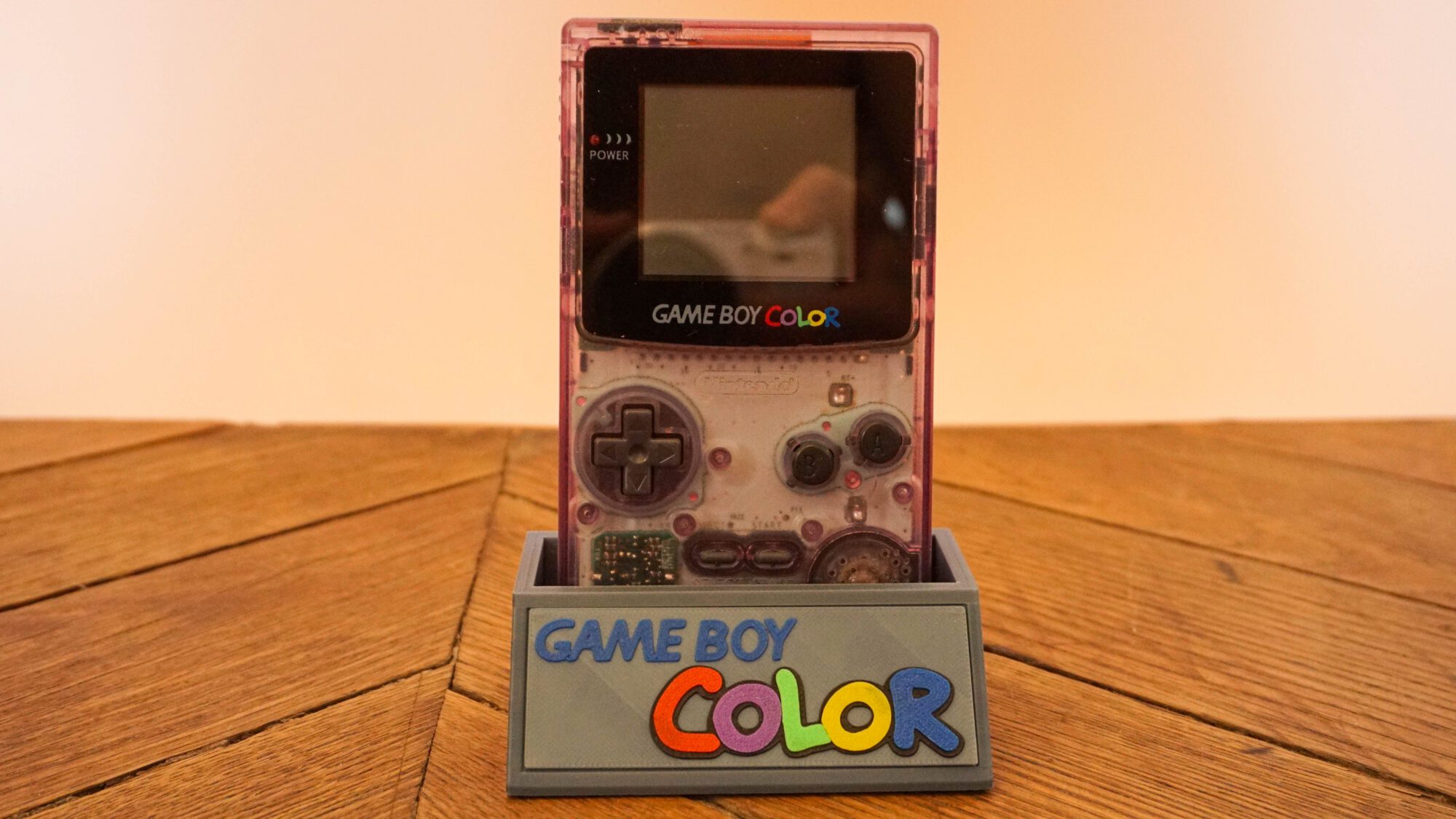Photo d'une Game Boy Color Transparente/Violette sur son socle, vue de face