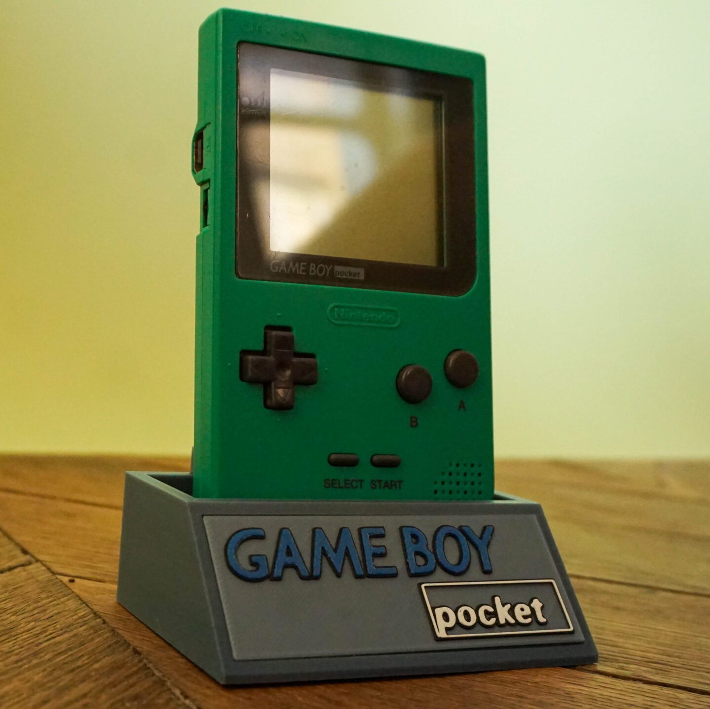 Photo d'une Game Boy Pocket Verte sur son socle, vue de 3/4