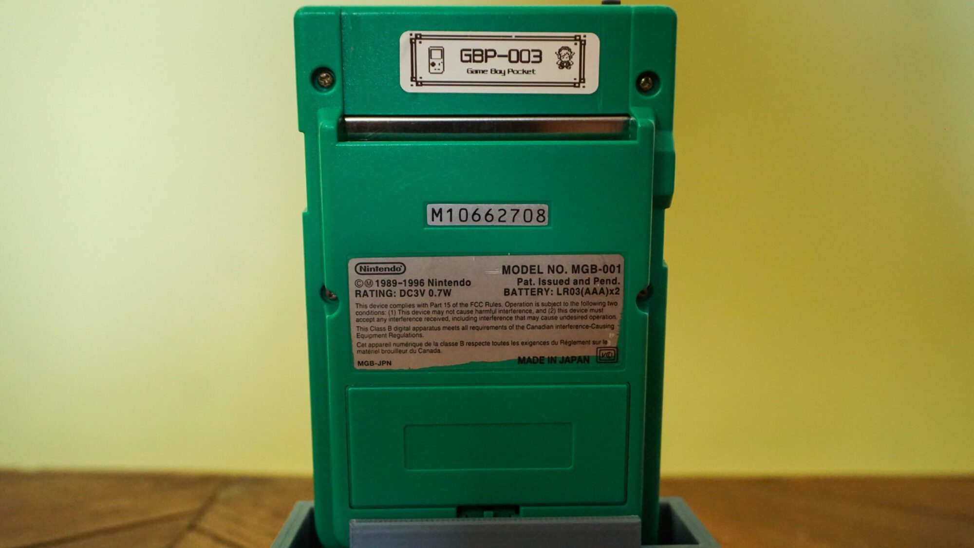 Photo d'une Game Boy Pocket Verte sur son socle, vue de dos