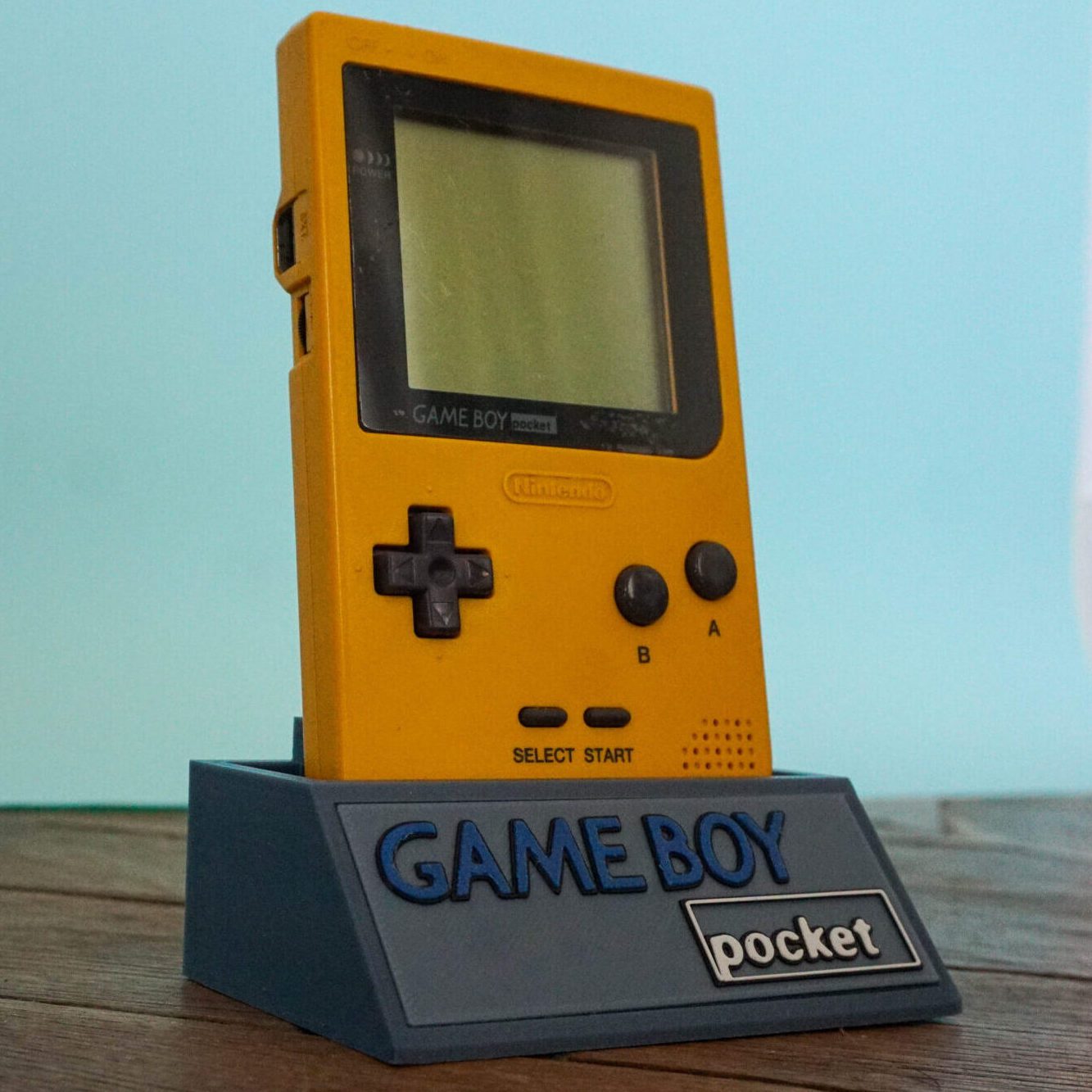 Photo d'une Game Boy Pocket Jaune sur son socle, vue de 3/4