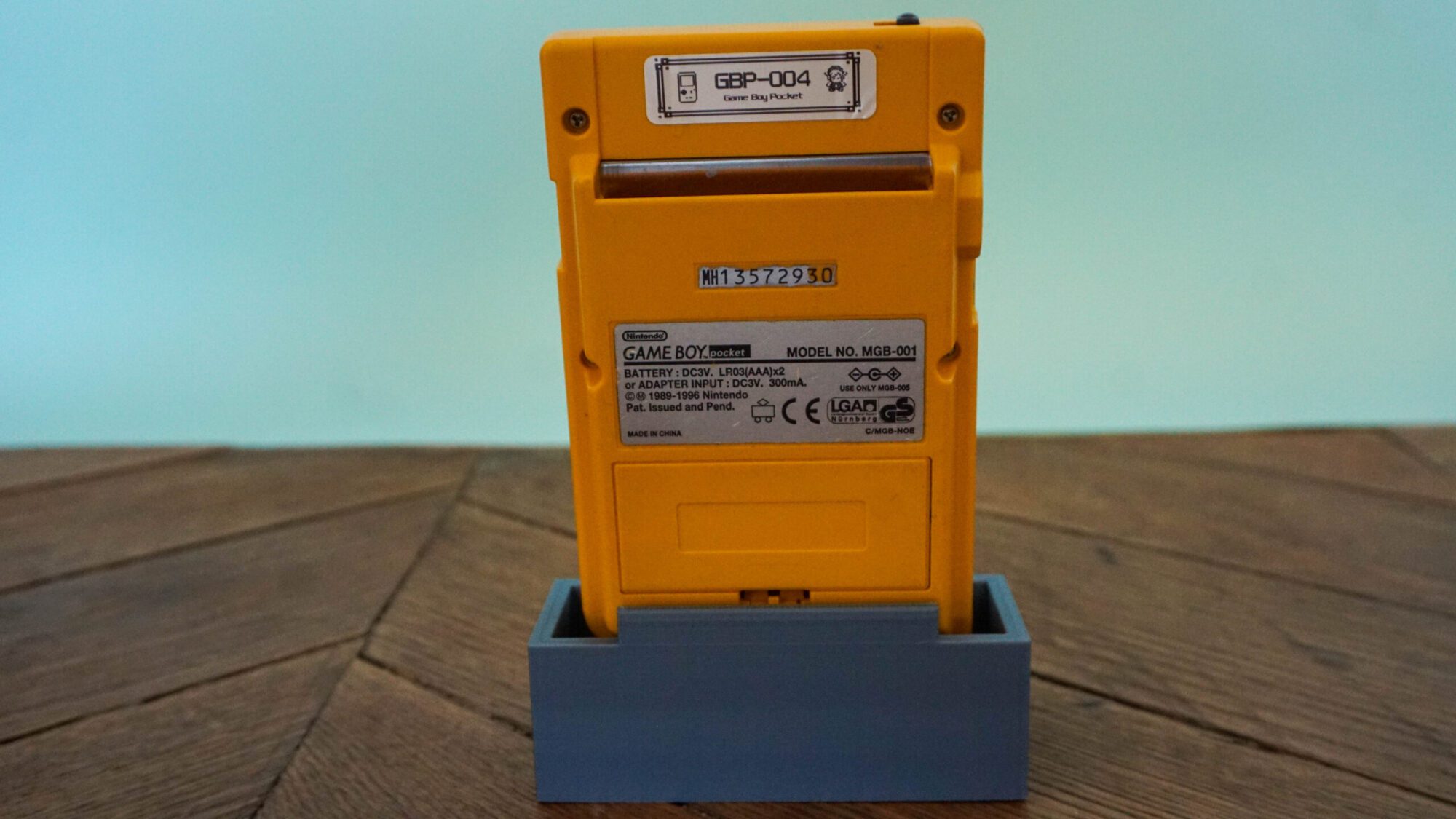 Photo d'une Game Boy Pocket Jaune sur son socle, vue de dos