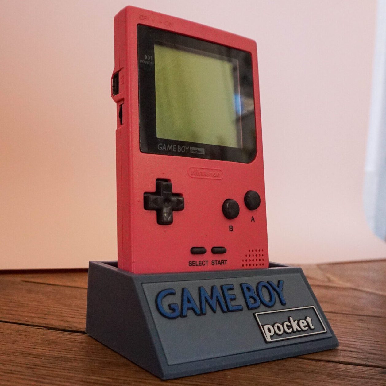Photo d'une Game Boy Pocket Rose restaurée sur son socle, vue de 3/4