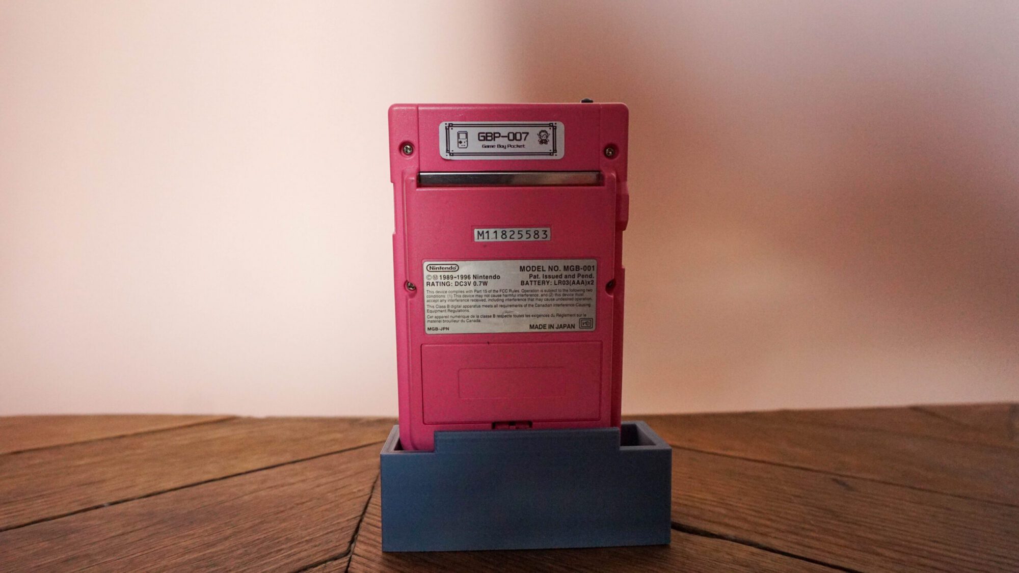 Photo d'une Game Boy Pocket Rose sur son socle, vue de dos