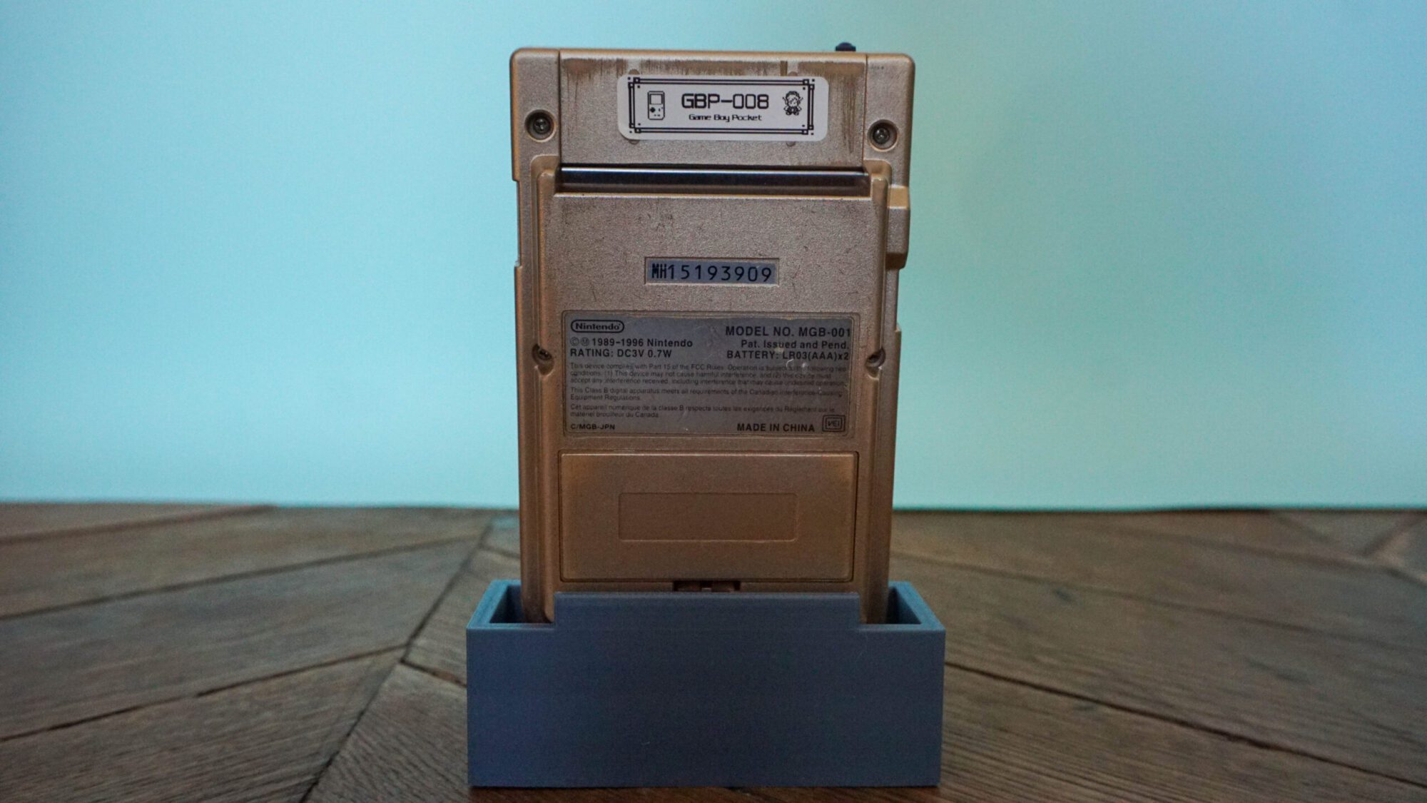 Photo d'une Game Boy Pocket Or sur son socle, vue de dos