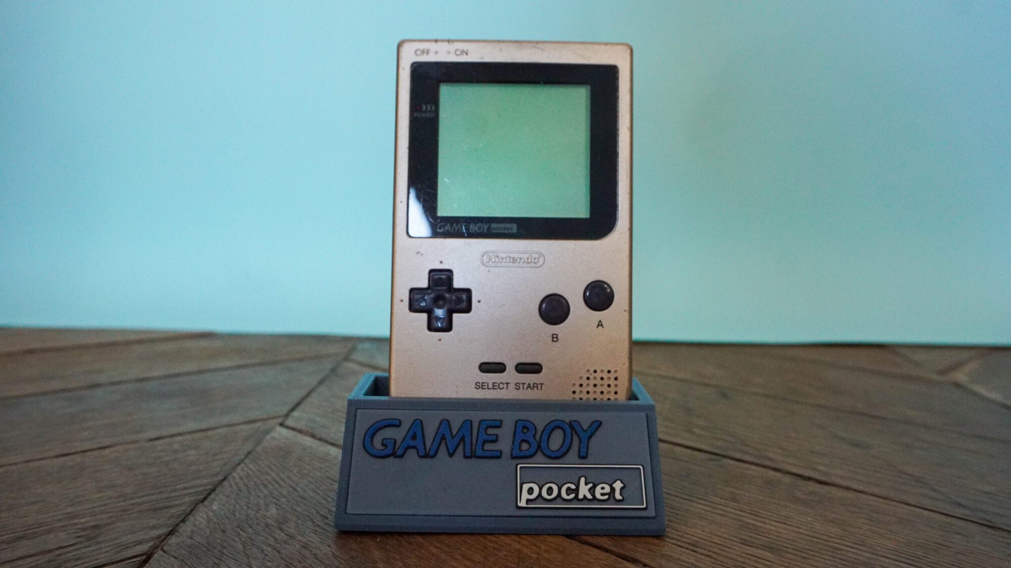 Photo d'une Game Boy Pocket Or sur son socle, vue de face
