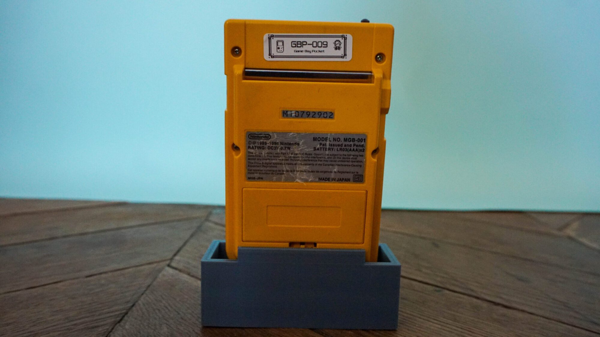Photo d'une Game Boy Pocket Jaune sur son socle, vue de dos