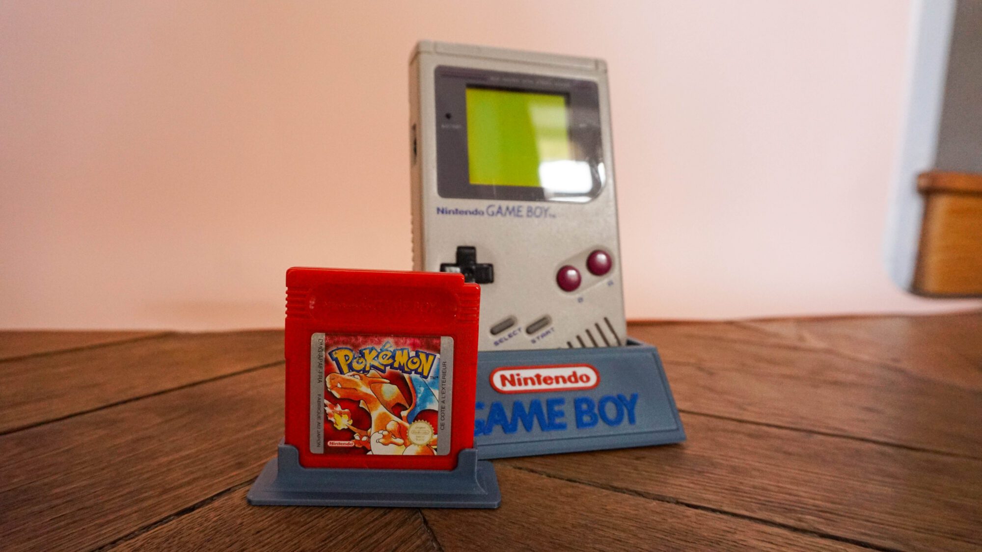 Photo d'une Game Boy Classic Grise sur son socle, vue de 3/4, avec le jeu Pokémon Rouge