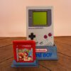 Photo d'une Game Boy Classic Grise sur son socle, vue de face, avec le jeu Pokémon Rouge