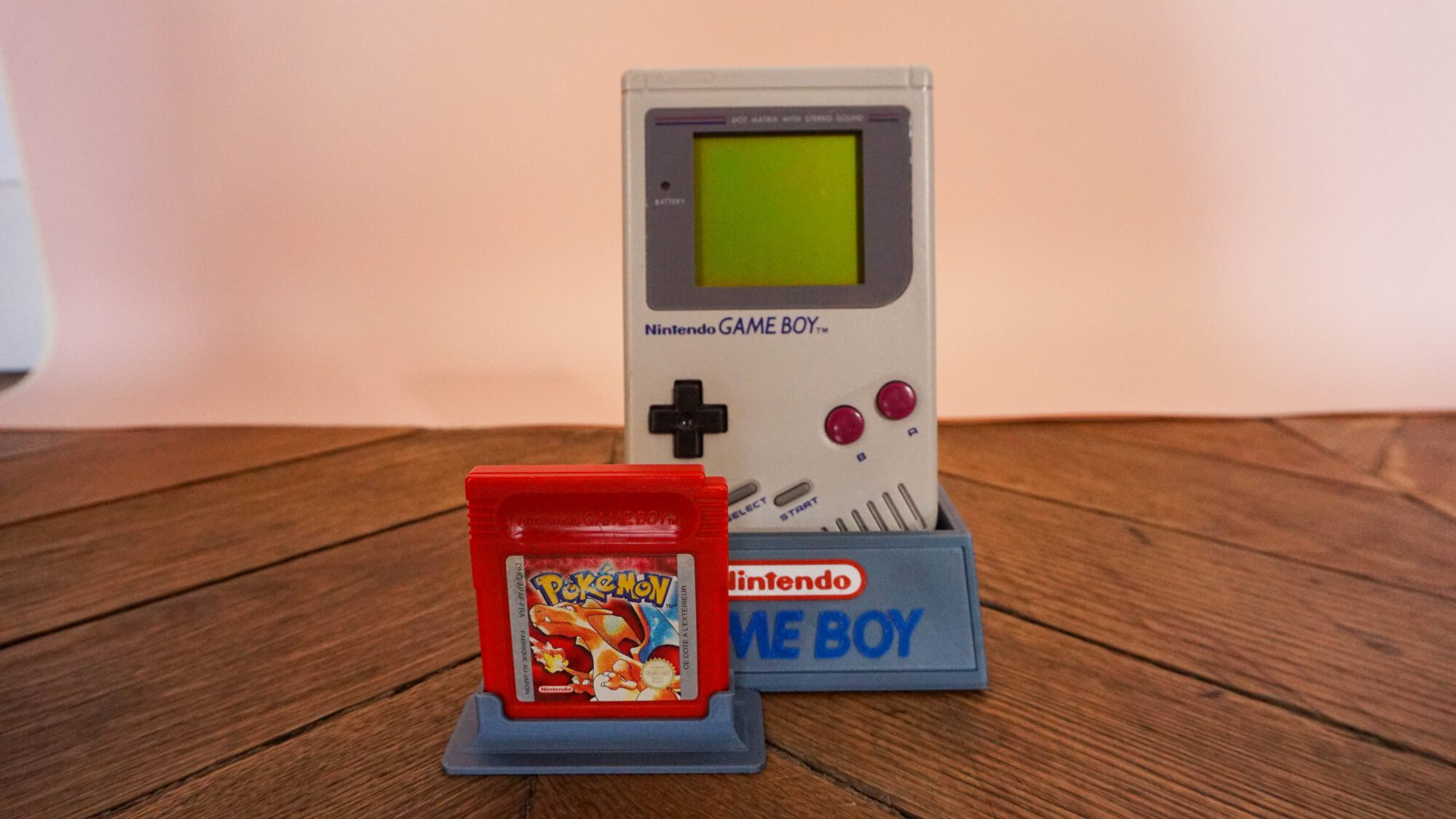 Photo d'une Game Boy Classic Grise sur son socle, vue de face, avec le jeu Pokémon Rouge