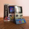 Photo d'une Game Boy Color Transparente sur son socle, vue de 3/4, avec sa boîte