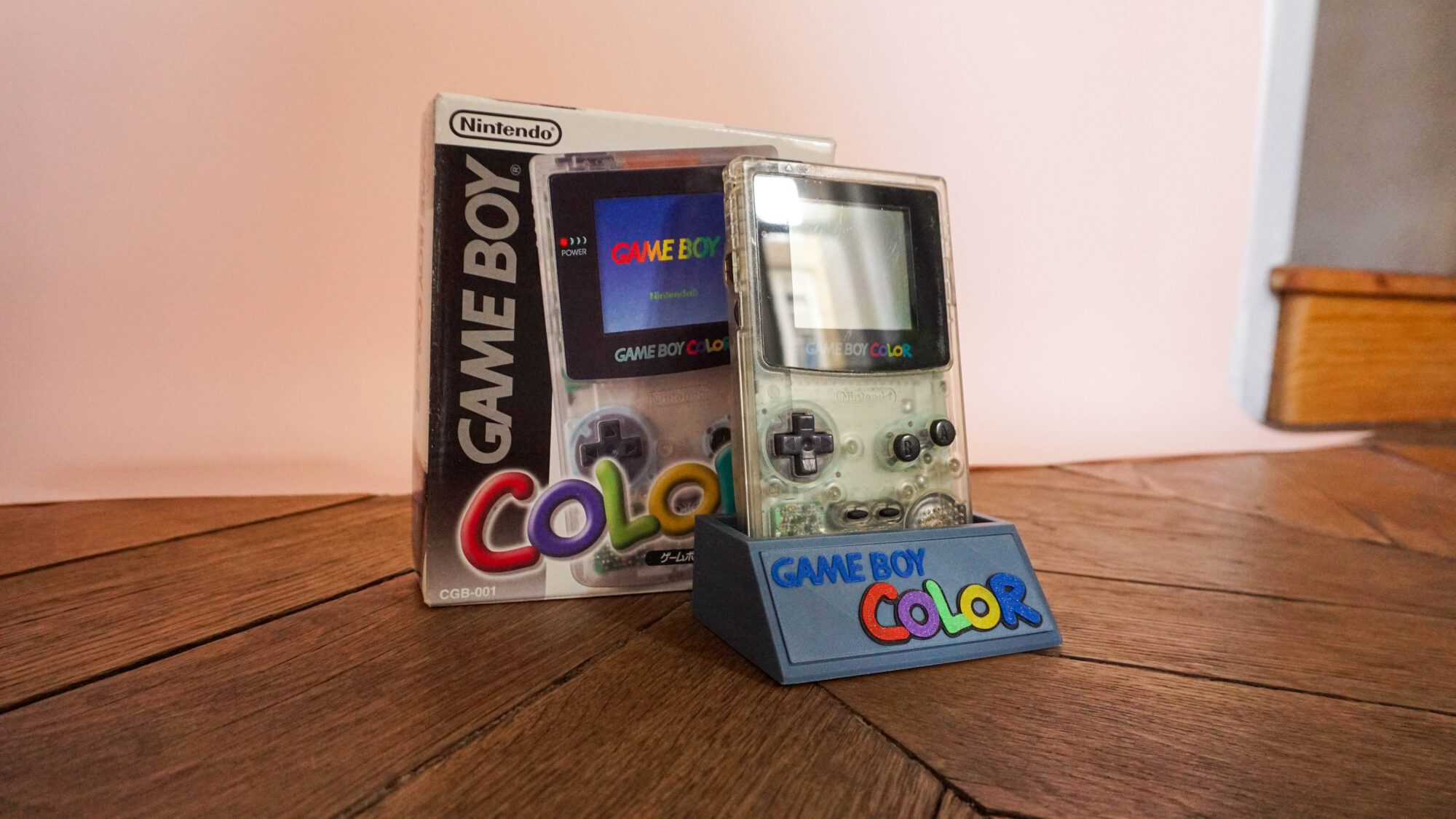 Photo d'une Game Boy Color Transparente sur son socle, vue de 3/4, avec sa boîte