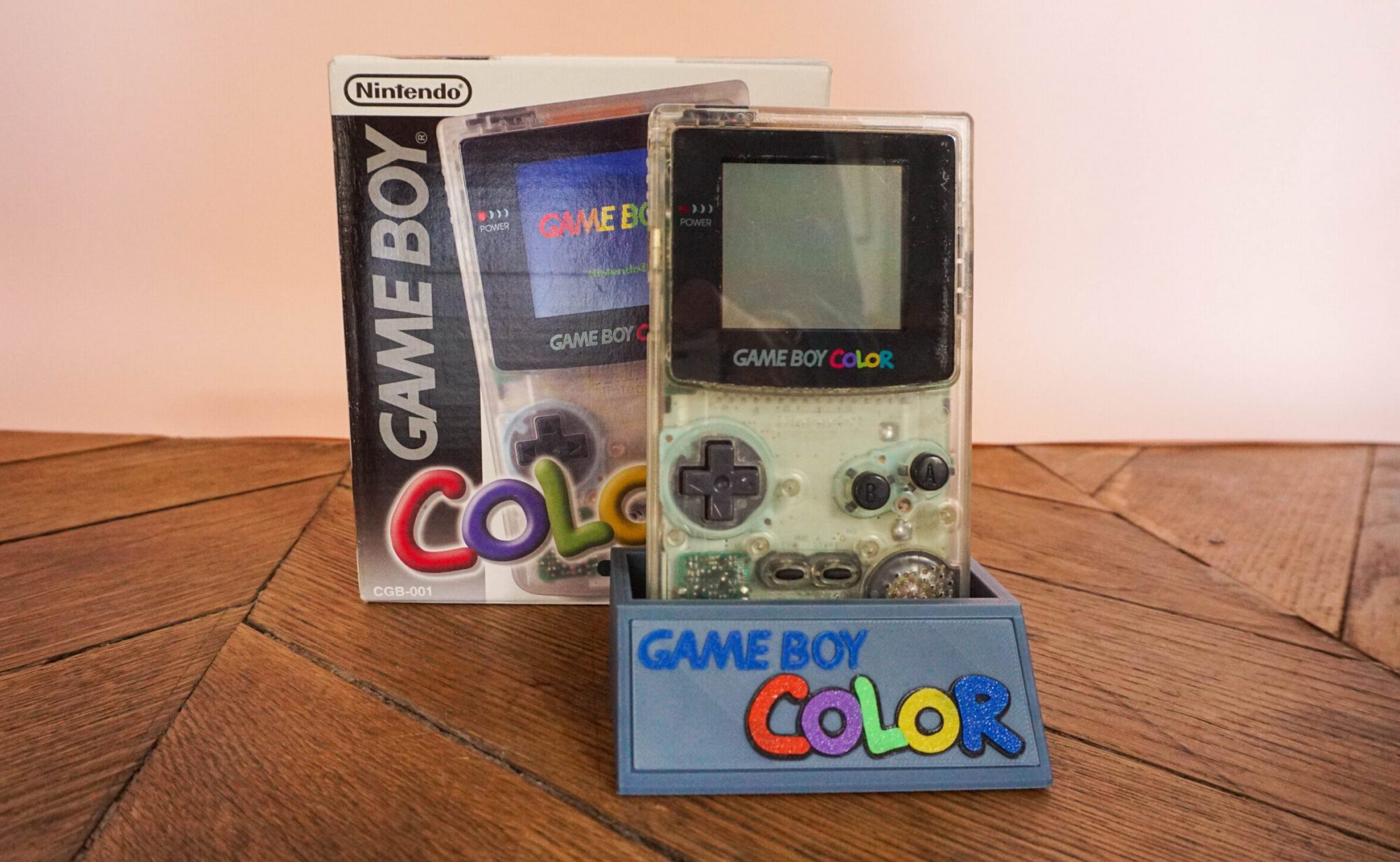 Photo d'une Game Boy Color Transparente sur son socle, vue de face, avec sa boîte