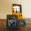 Photo d'une Game Boy Color Jaune sur son socle, vue de 3/4, avec le jeu Zelda Oracles of Ages