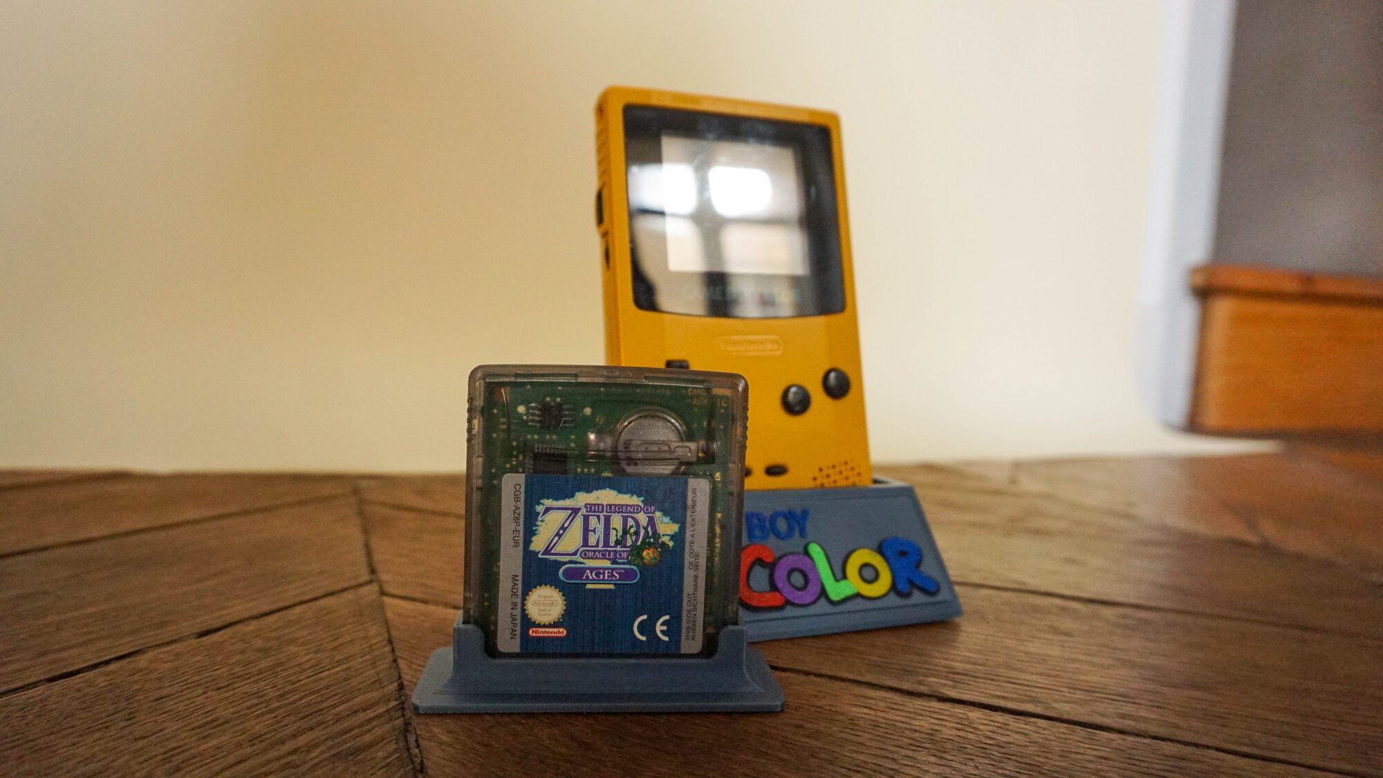Photo d'une Game Boy Color Jaune sur son socle, vue de 3/4, avec le jeu Zelda Oracles of Ages