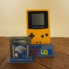 Photo d'une Game Boy Color Jaune sur son socle, vue de face, avec le jeu Zelda Oracles of Ages
