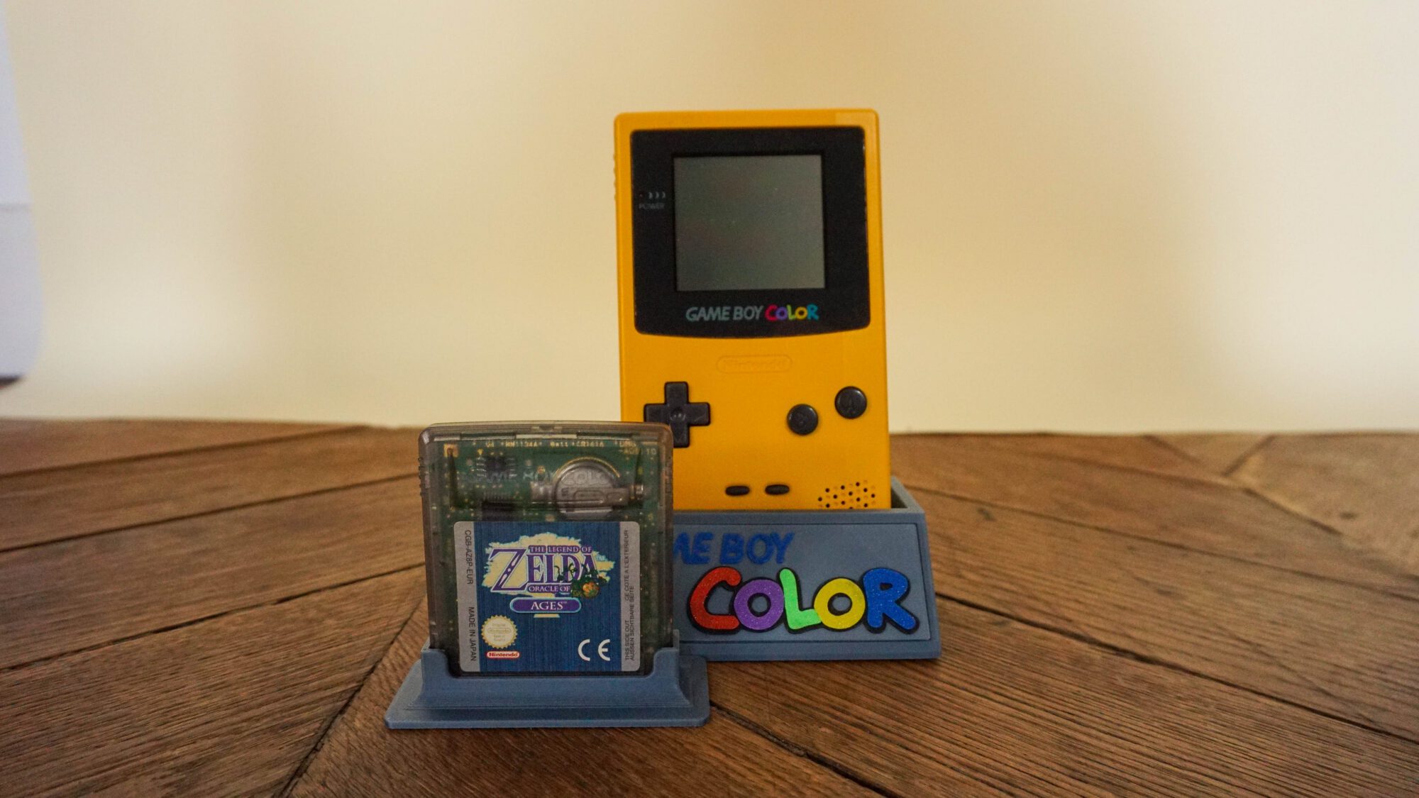 Photo d'une Game Boy Color Jaune sur son socle, vue de face, avec le jeu Zelda Oracles of Ages