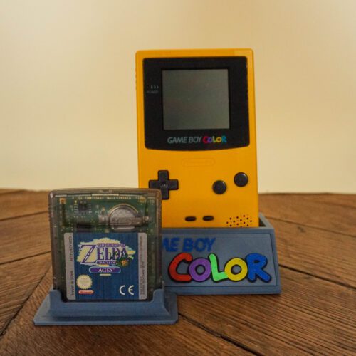 Photo d'une Game Boy Color Jaune sur son socle, vue de face, avec le jeu Zelda Oracles of Ages
