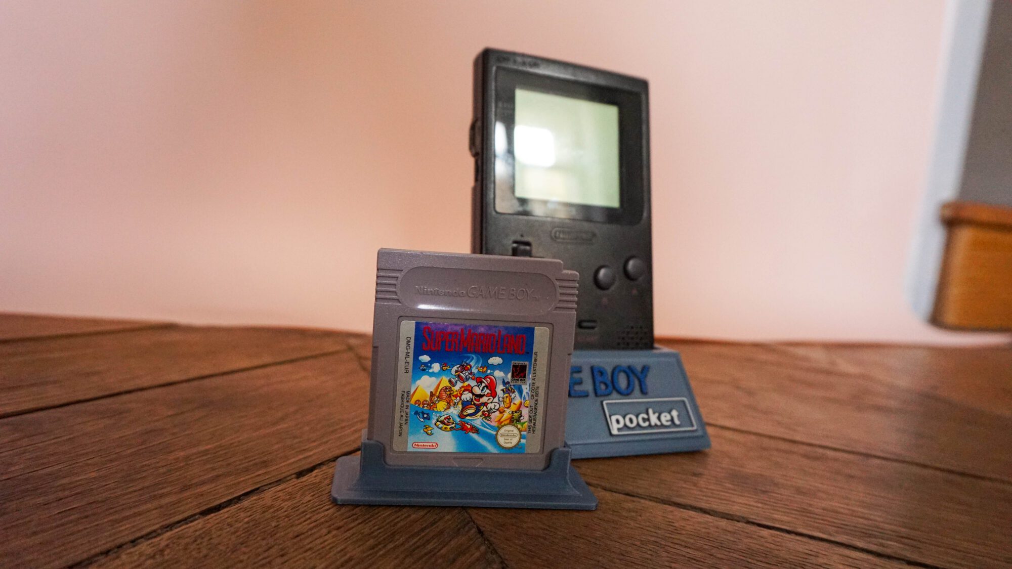 Photo d'une Game Boy Pocket Noire sur son socle, vue de 3/4, avec le jeu Super Mario Land